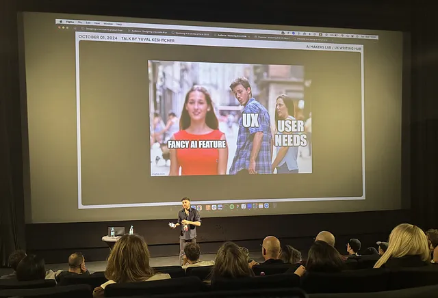 Speaker Yuval Keshtcher stands in front of the audience, the screen on his back shows the image of a meme that says “FANCY AI FEATURE, UX, USER NEEDS”